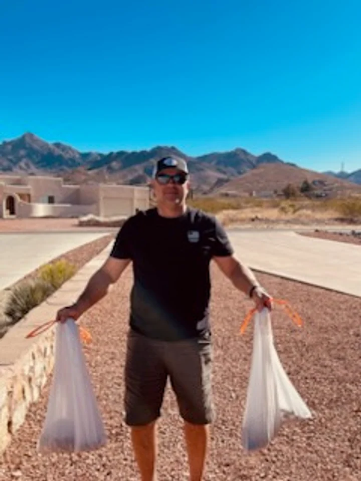 Cruces Scoopers crew member carrying collected waste on a Las Cruces route near the Organ Mountains